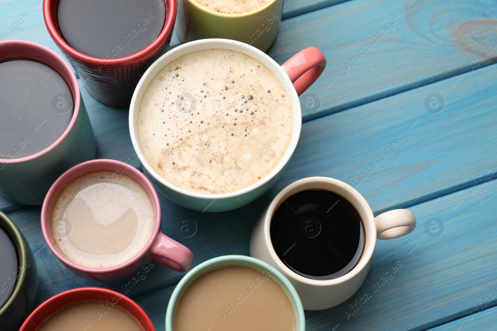 Photo of Many cups of different coffee drinks on light blue wooden table, above view