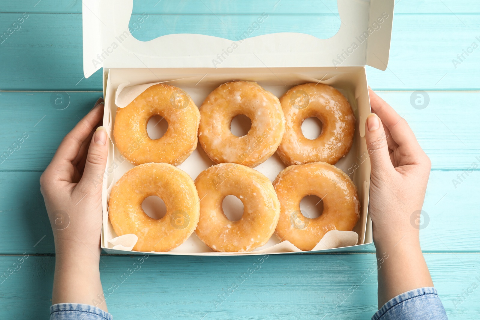 Photo of Woman with box of delicious donuts at light blue wooden table, top view