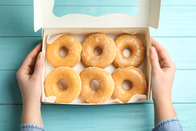 Photo of Woman with box of delicious donuts at light blue wooden table, top view