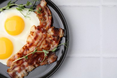 Fried eggs, bacon and microgreens on white tiled table, top view. Space for text