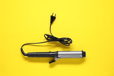 Photo of Curling iron on yellow background, top view