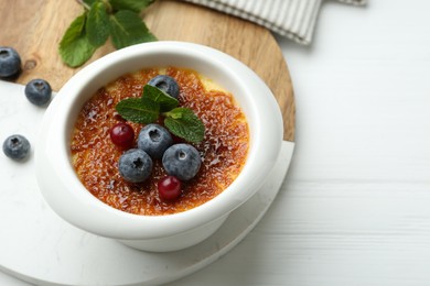 Delicious creme brulee with berries and mint in bowl on white table, closeup. Space for text