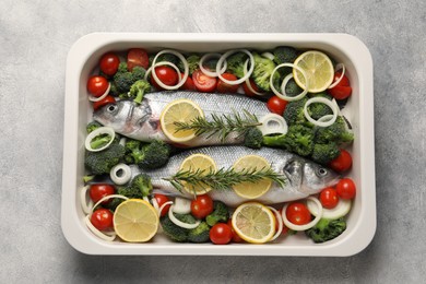 Photo of Raw fish with vegetables and lemon in baking dish on grey textured table, top view