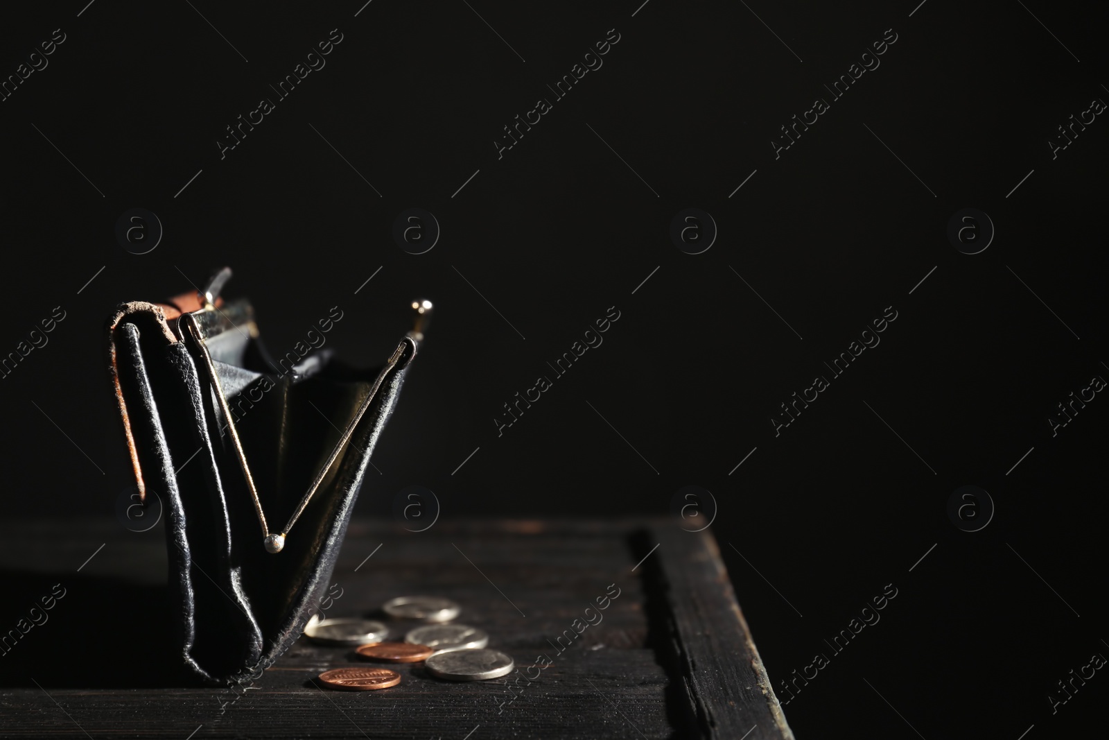 Photo of Wallet and coins on table against dark background with space for text. Poverty concept