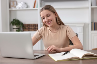 Photo of Online learning. Smiling teenage girl with laptop at wooden table indoors