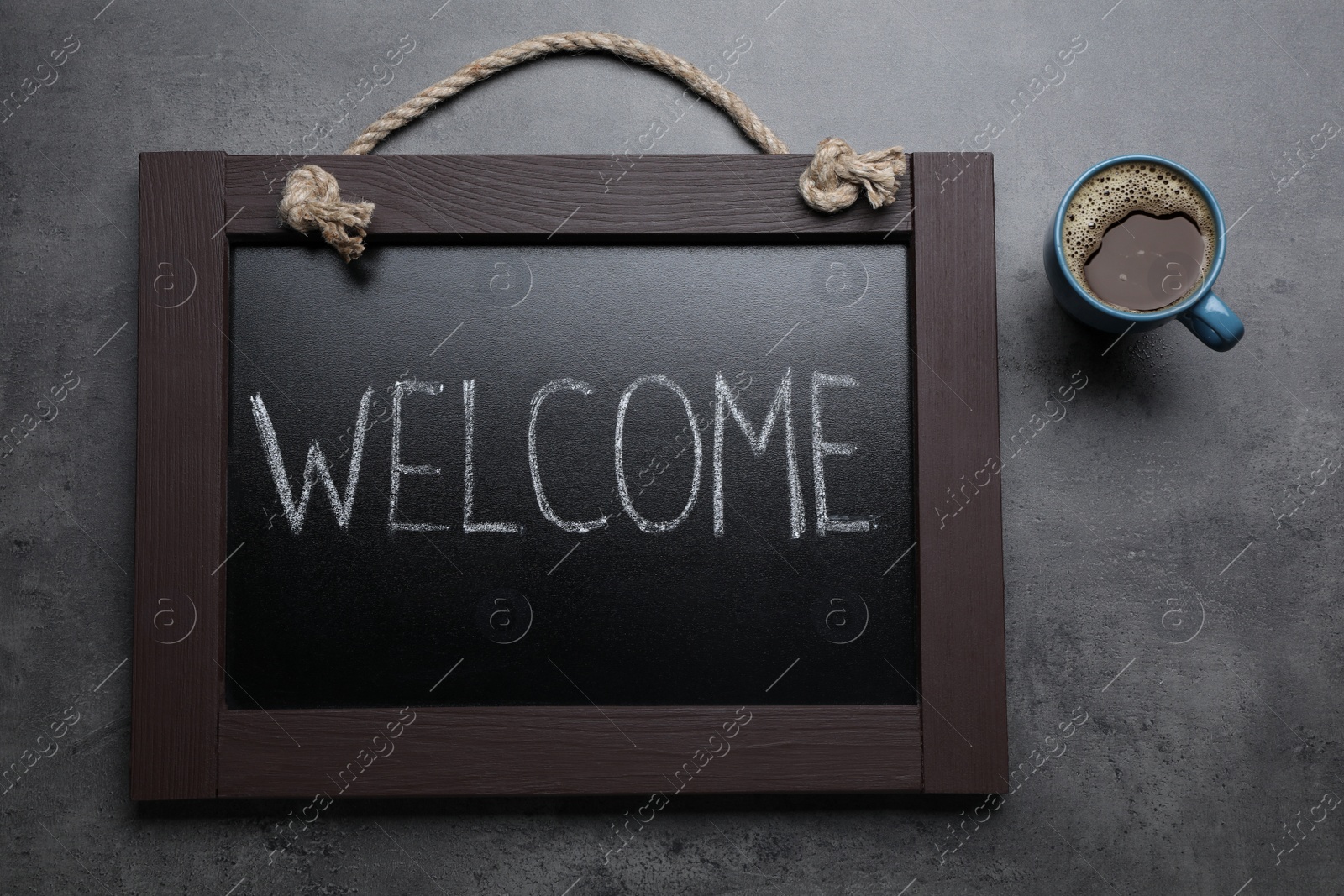 Photo of Blackboard with word Welcome and cup of coffee on grey table, flat lay