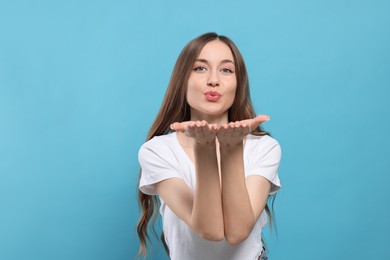 Beautiful young woman blowing kiss on light blue background