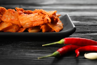 Photo of Delicious kimchi with Chinese cabbage, red chili peppers and garlic on black wooden table, closeup