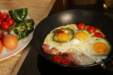 Cooking eggs with bacon, tomatoes and pepper in frying pan
