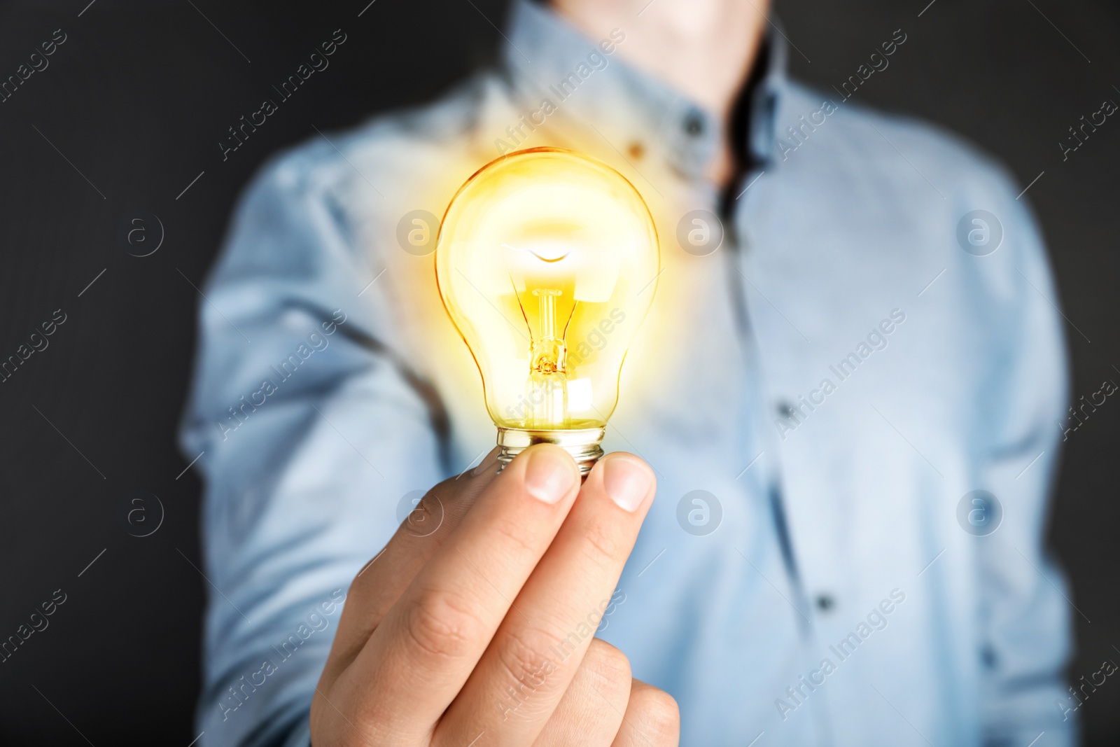 Image of Glow up your ideas. Man holding light bulb on dark background, closeup