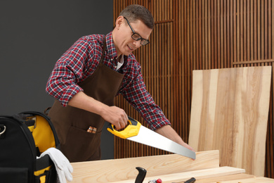 Photo of Carpenter working with hand saw at table indoors
