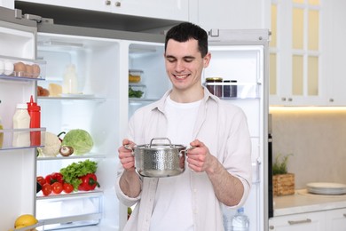 Happy man holding pot near refrigerator in kitchen