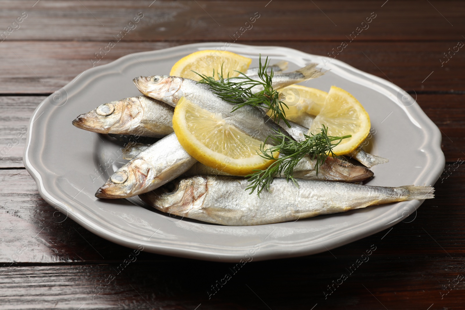 Photo of Fresh raw sprats, dill and cut lemon on wooden table, closeup