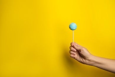 Woman holding bright delicious cake pop on color background, closeup. Space for text