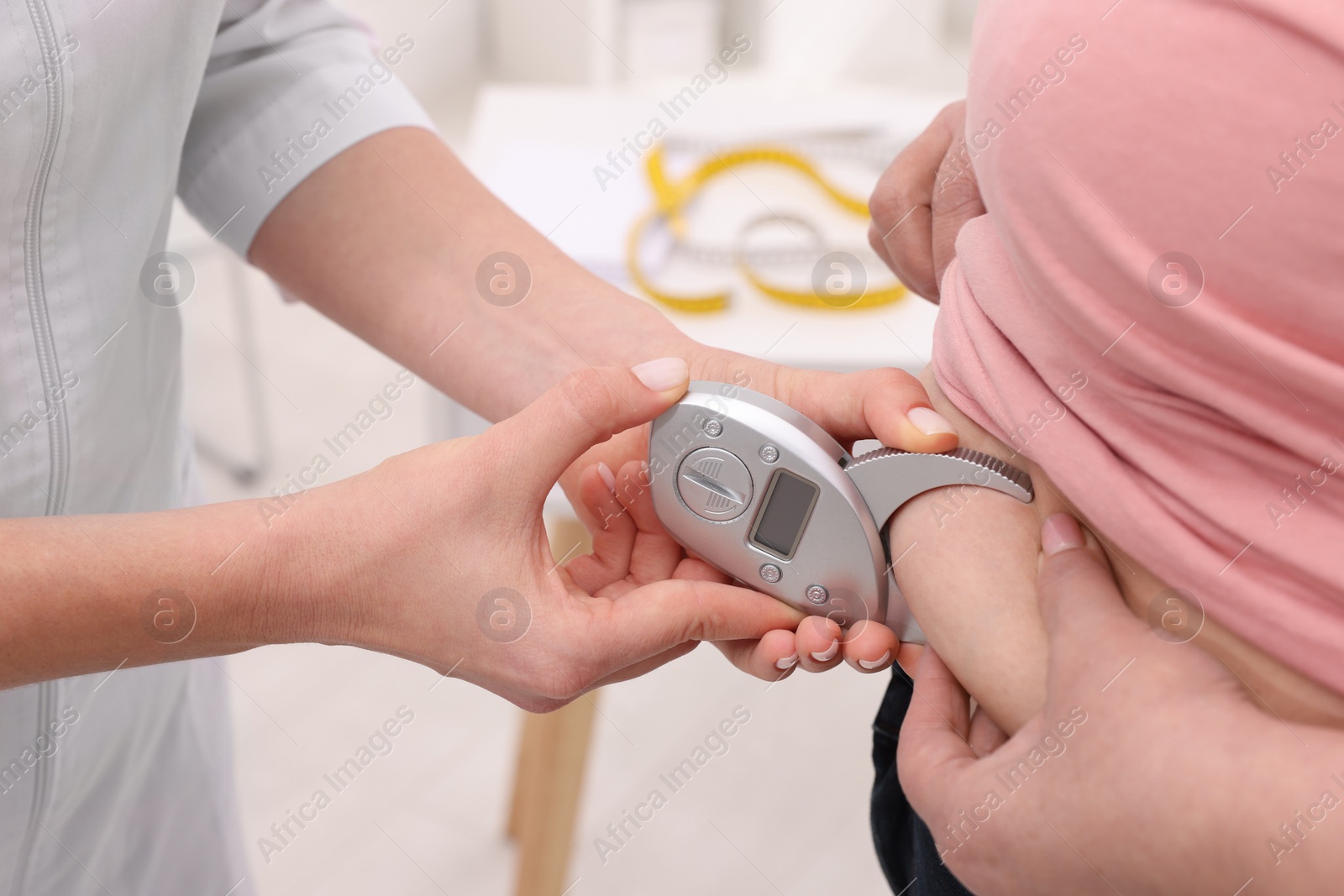 Photo of Nutritionist measuring overweight woman's body fat layer with caliper in clinic, closeup