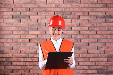 Female industrial engineer in uniform with clipboard on brick wall background. Safety equipment