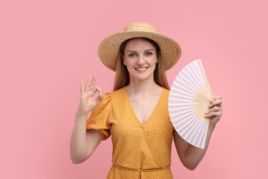 Happy woman with hand fan showing OK gesture on pink background