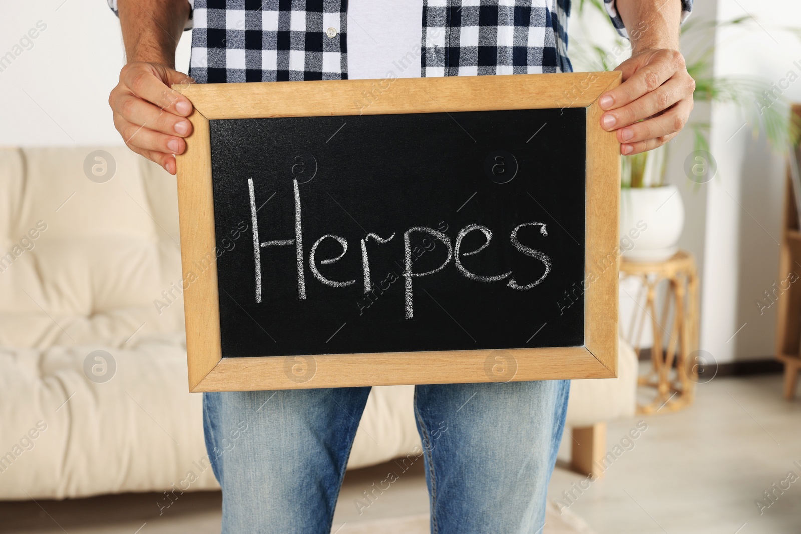 Photo of Man holding small chalkboard with word Herpes at home, closeup
