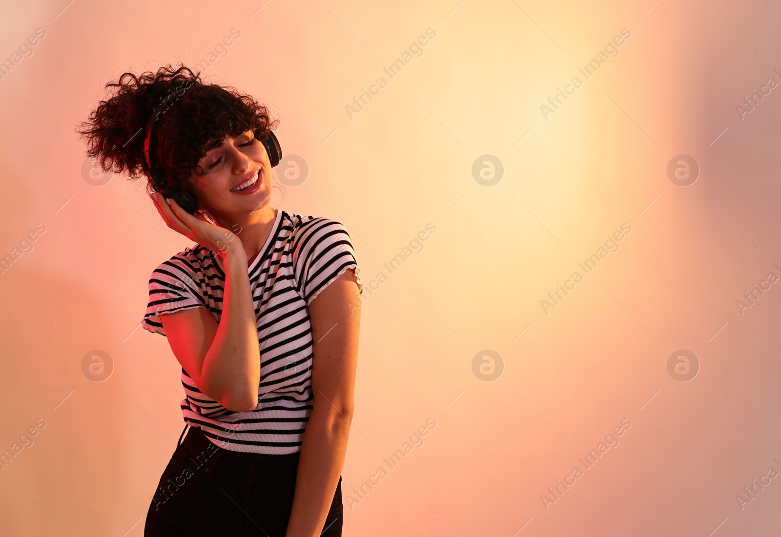 Photo of Beautiful young woman listening to music with headphones on color background in neon lights. Space for text