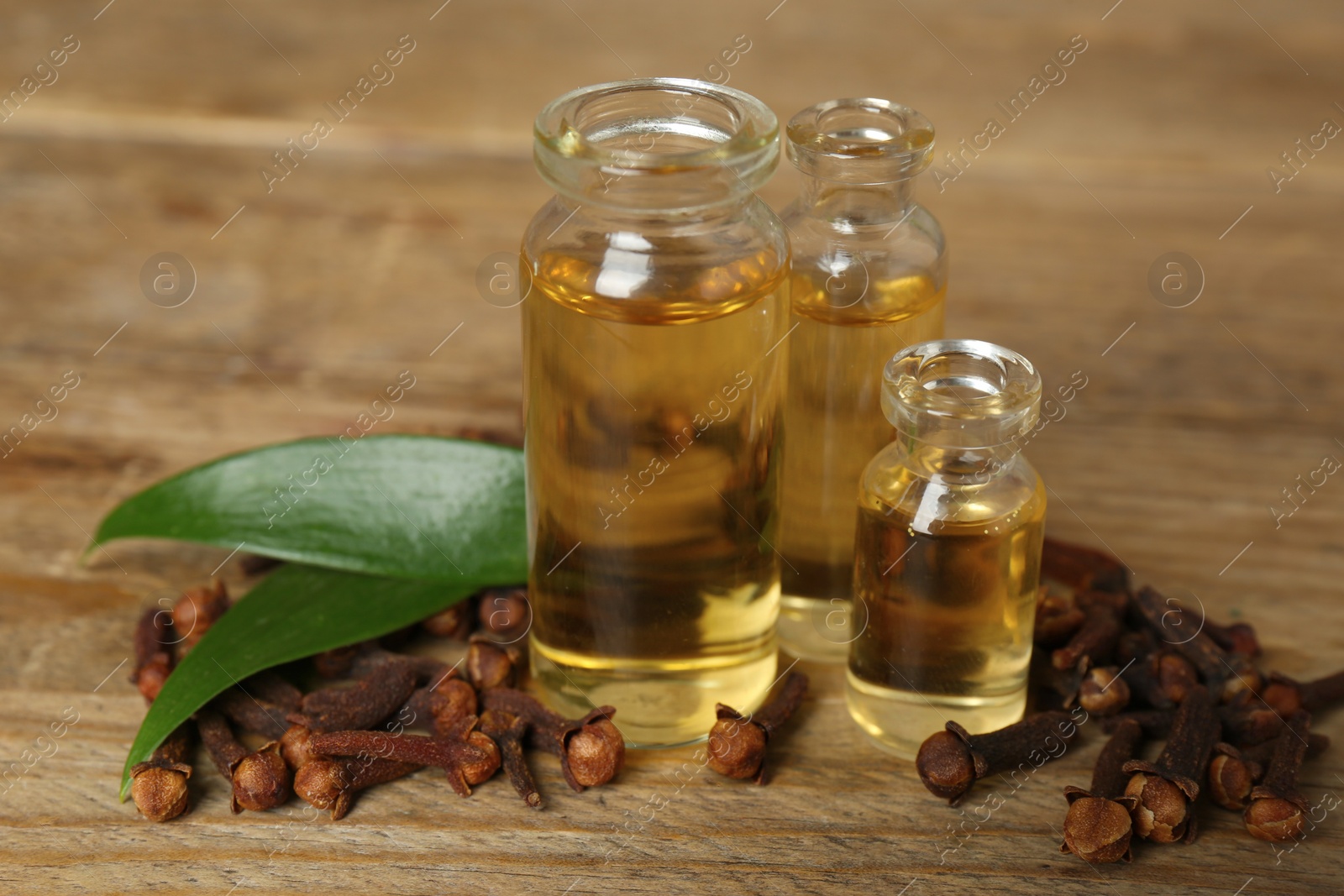 Photo of Essential oil, dried cloves and leaves on wooden table, closeup