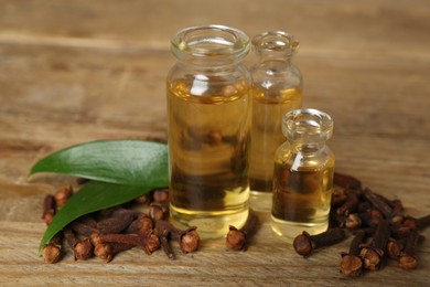 Essential oil, dried cloves and leaves on wooden table, closeup