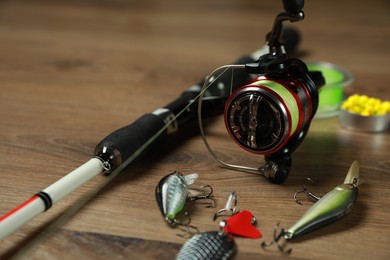 Fishing rod with spinning reel and baits on wooden background, closeup