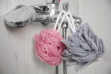 Photo of Colorful shower puffs hanging on faucet in bathroom, closeup