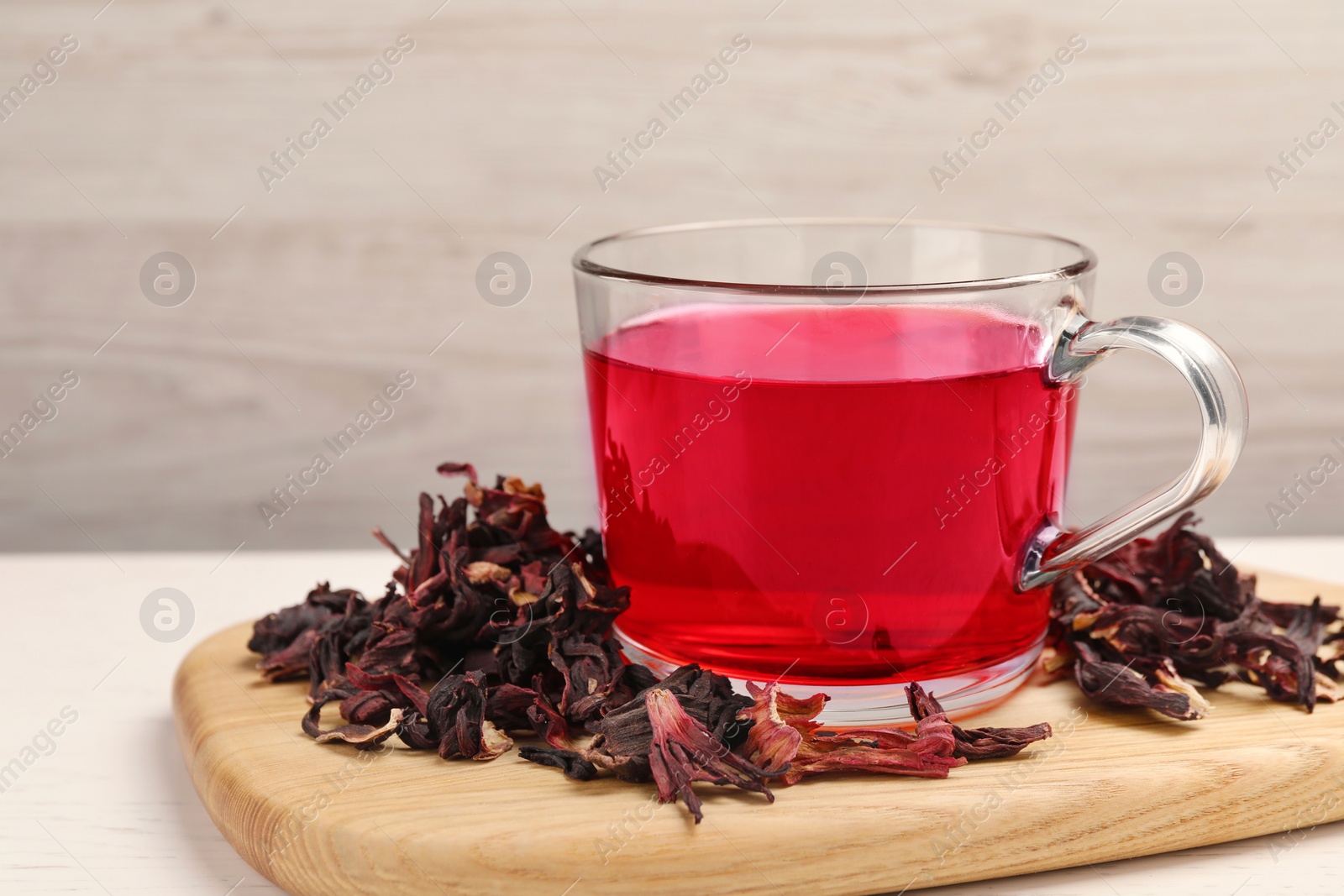 Photo of Cup of fresh hibiscus tea and dry flower leaves on wooden board