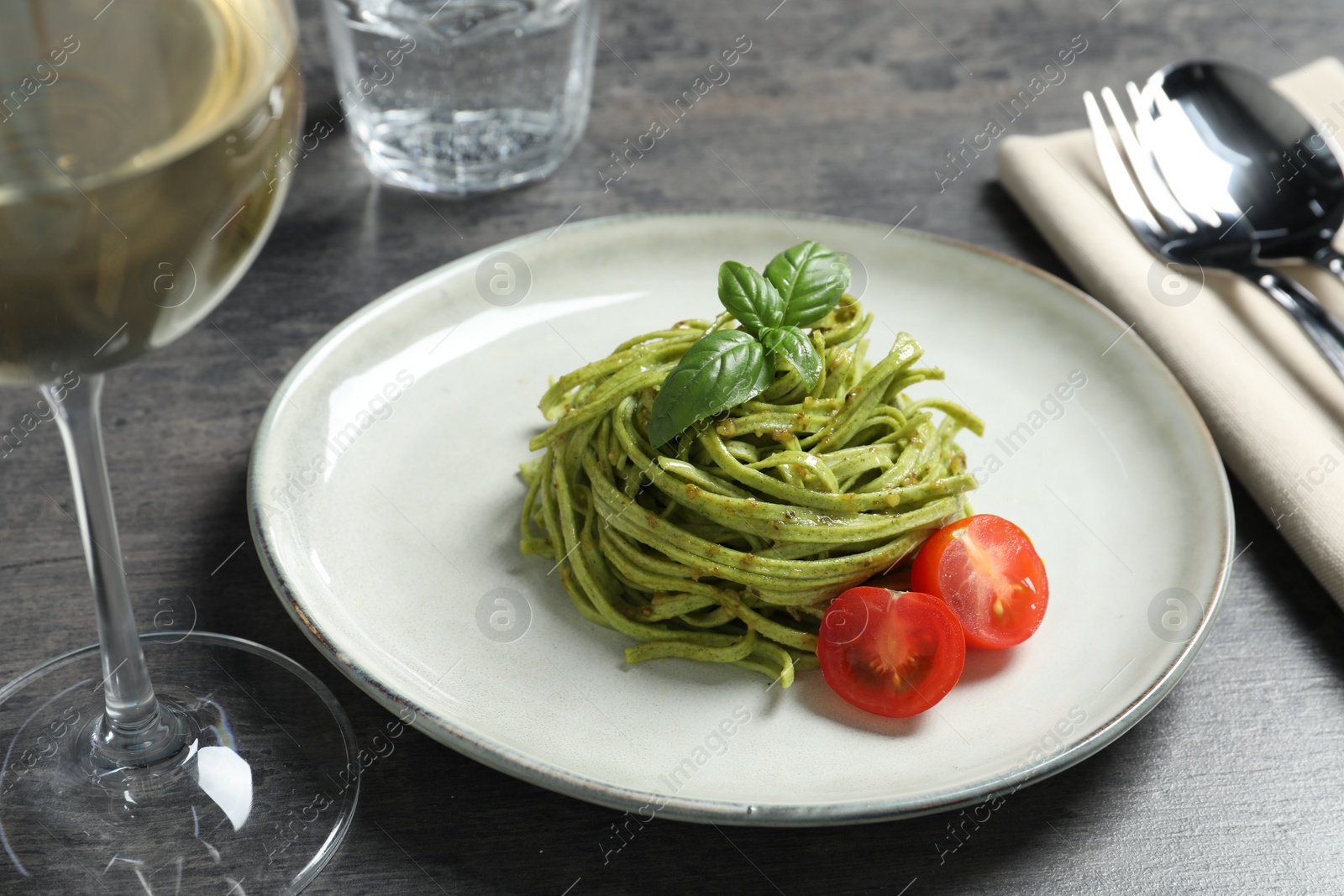 Photo of Tasty tagliatelle with spinach and tomatoes served on grey table, closeup. Exquisite presentation of pasta dish