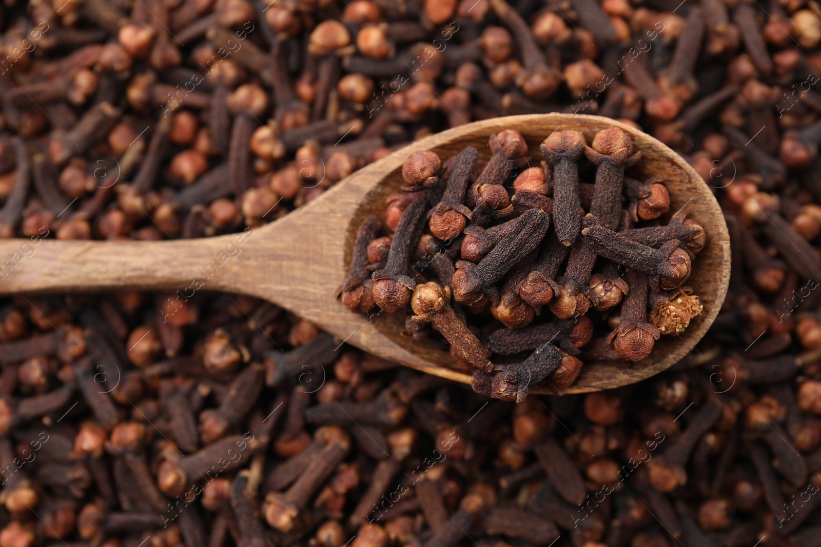 Photo of Many aromatic cloves and wooden spoon as background, top view