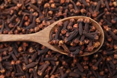 Photo of Many aromatic cloves and wooden spoon as background, top view