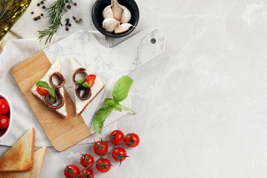 Photo of Delicious sandwiches with cream cheese, anchovies and tomatoes on light grey table, flat lay. Space for text