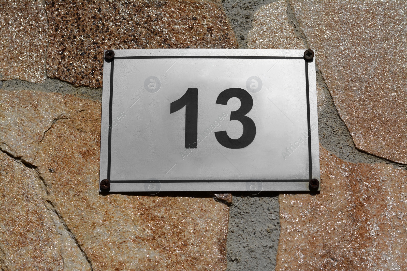 Photo of Plate with number 13 on textured stone wall, closeup