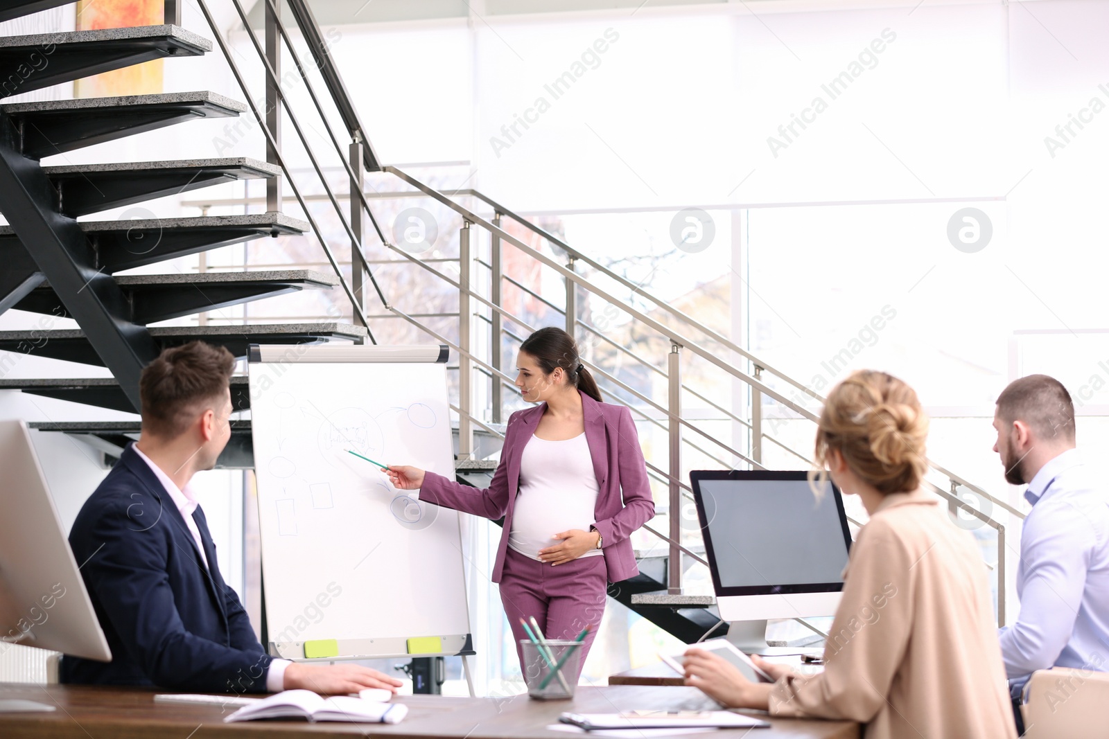 Photo of Young pregnant woman giving presentation to colleagues at workplace