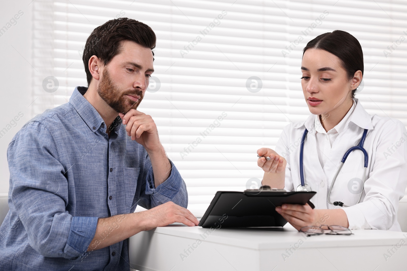 Photo of Doctor with clipboard consulting patient during appointment in clinic