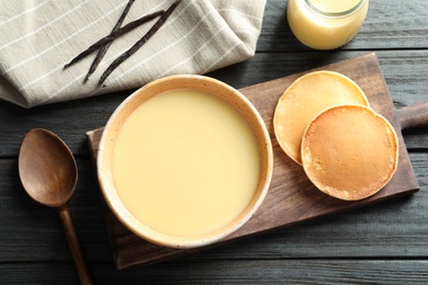 Photo of Bowl of condensed milk and pancakes served on wooden table, top view. Dairy products