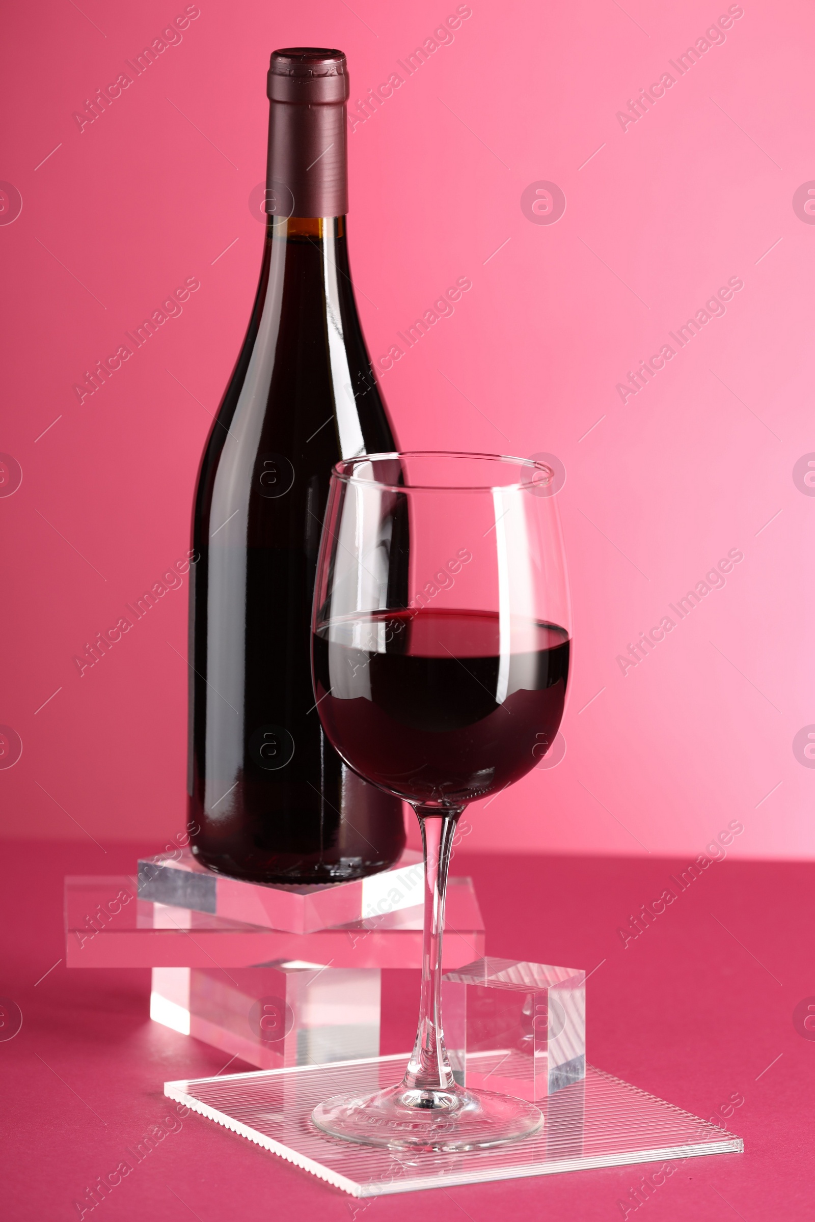 Photo of Stylish presentation of delicious red wine in bottle and glass on pink background