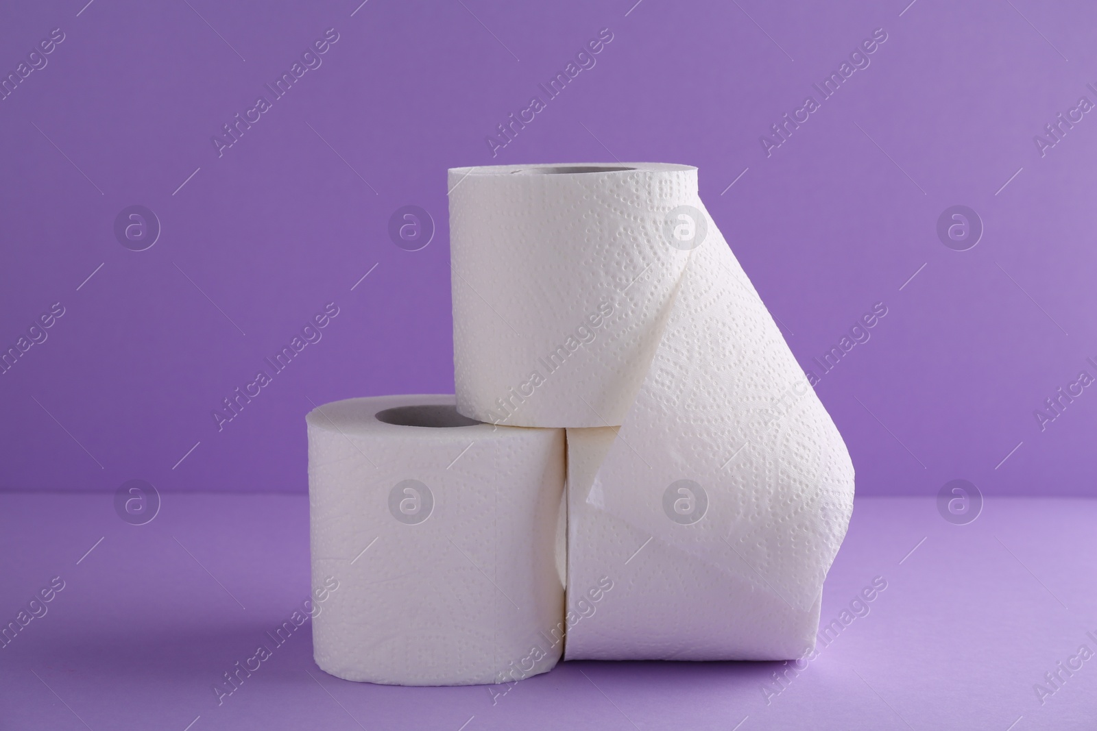 Photo of Soft toilet paper rolls on violet background, closeup