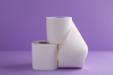 Photo of Soft toilet paper rolls on violet background, closeup