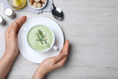 Photo of Woman with bowl of delicious asparagus soup at white wooden table, top view. Space for text