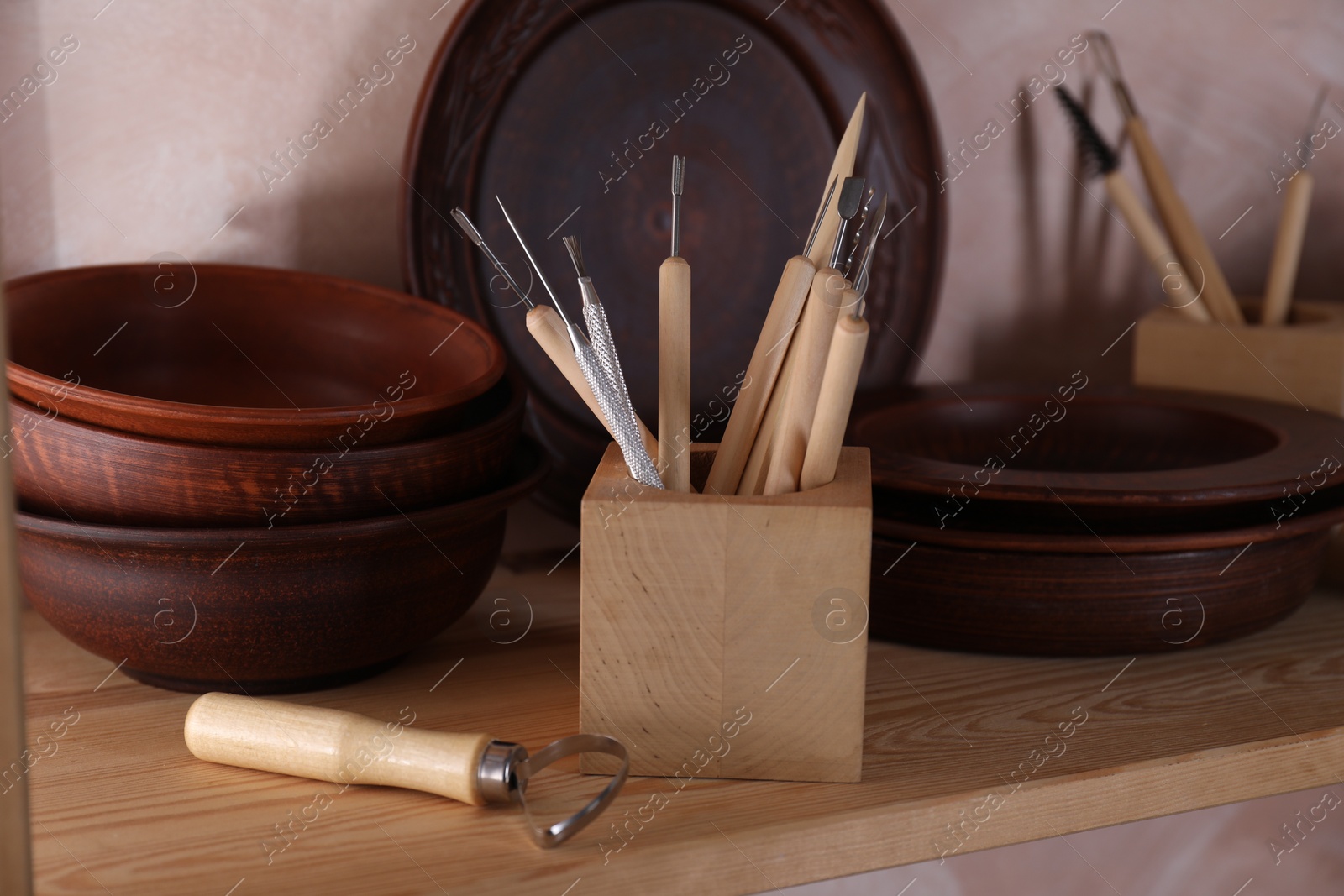 Photo of Set of different crafting tools and clay dishes on wooden rack in workshop