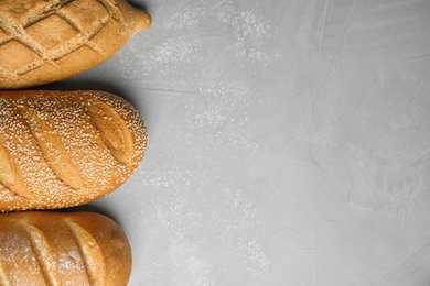 Loaves of different breads on grey background, flat lay. Space for text