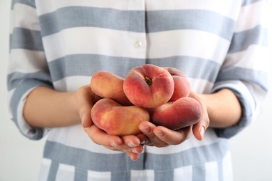 Photo of Woman holding heap of fresh ripe donut peaches on light background, closeup