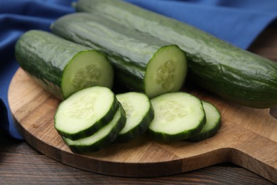 Fresh whole and cut cucumbers on wooden table, closeup