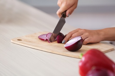 Photo of Young woman cutting onion at table, closeup