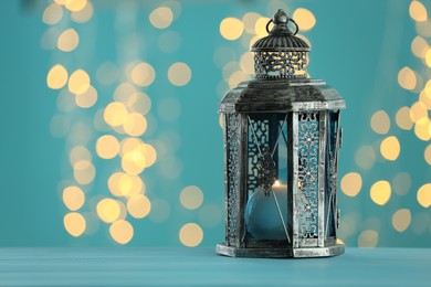 Photo of Traditional Arabic lantern on table against light blue background with blurred lights. Space for text