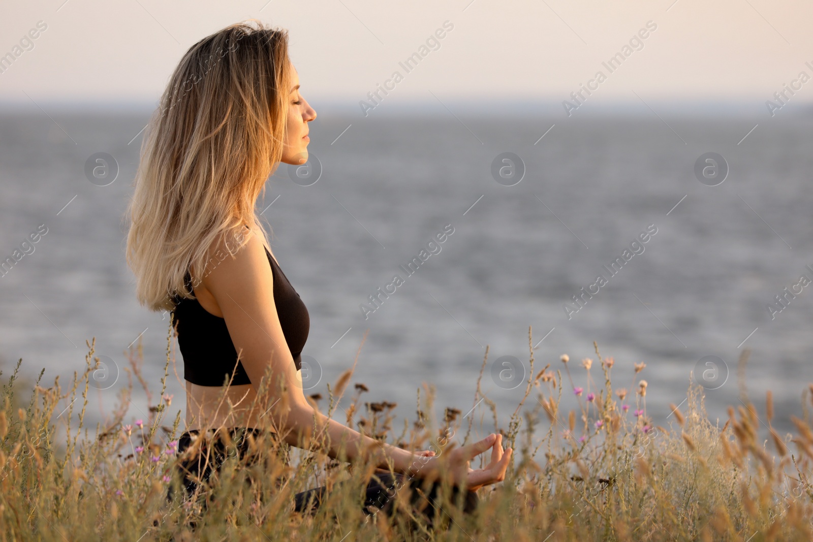 Photo of Young woman meditating near river on sunny day, space for text