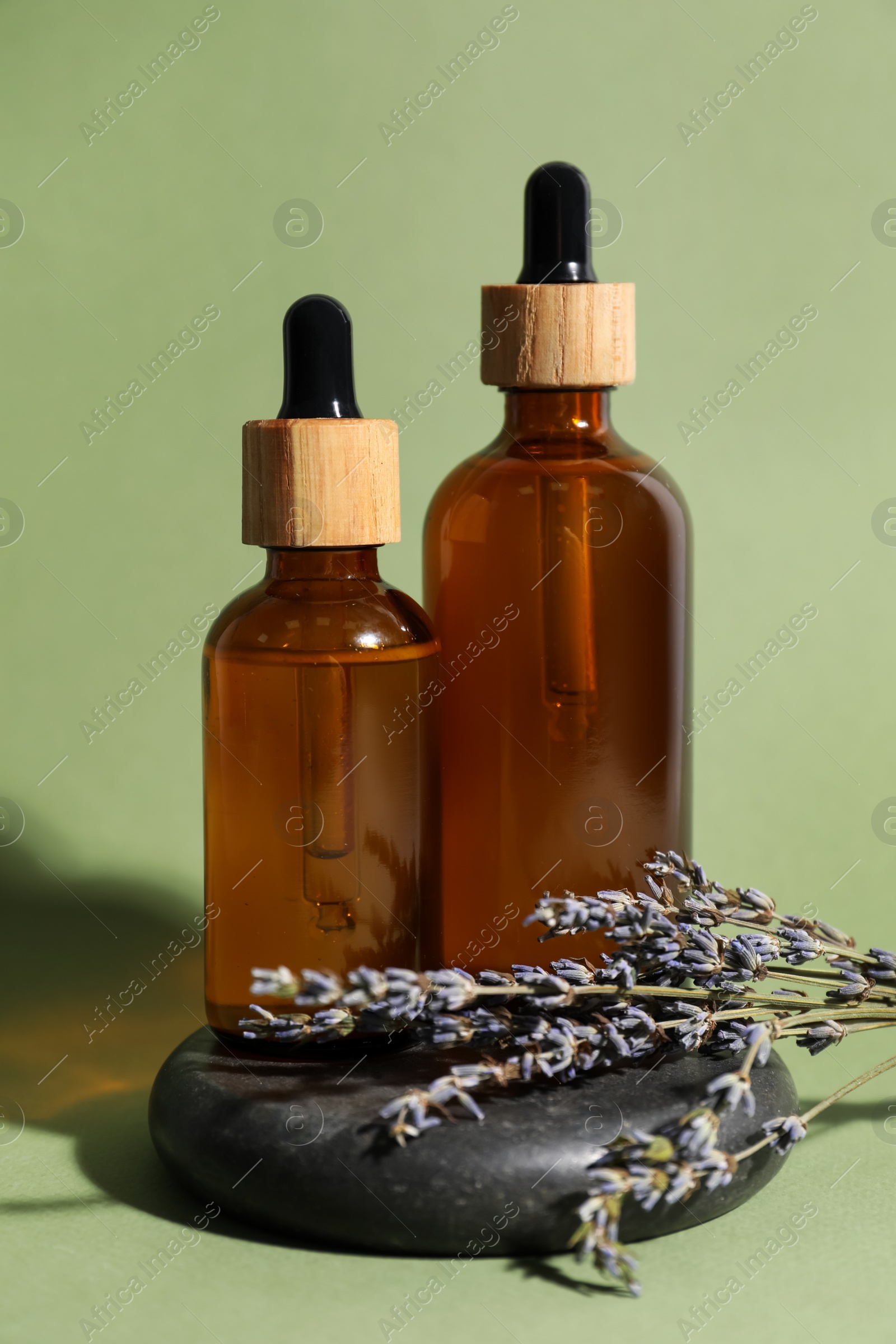 Photo of Composition with bottles of face serum, spa stone and beautiful flowers on light green background