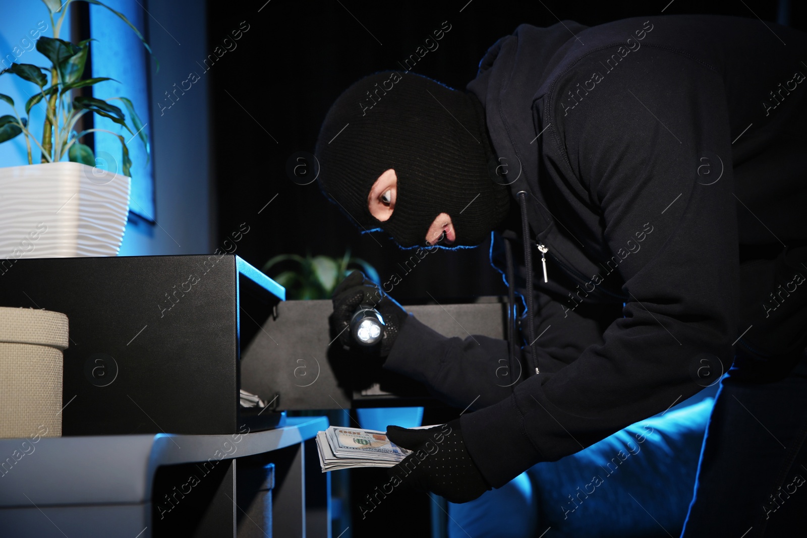 Photo of Thief taking money out of steel safe indoors at night