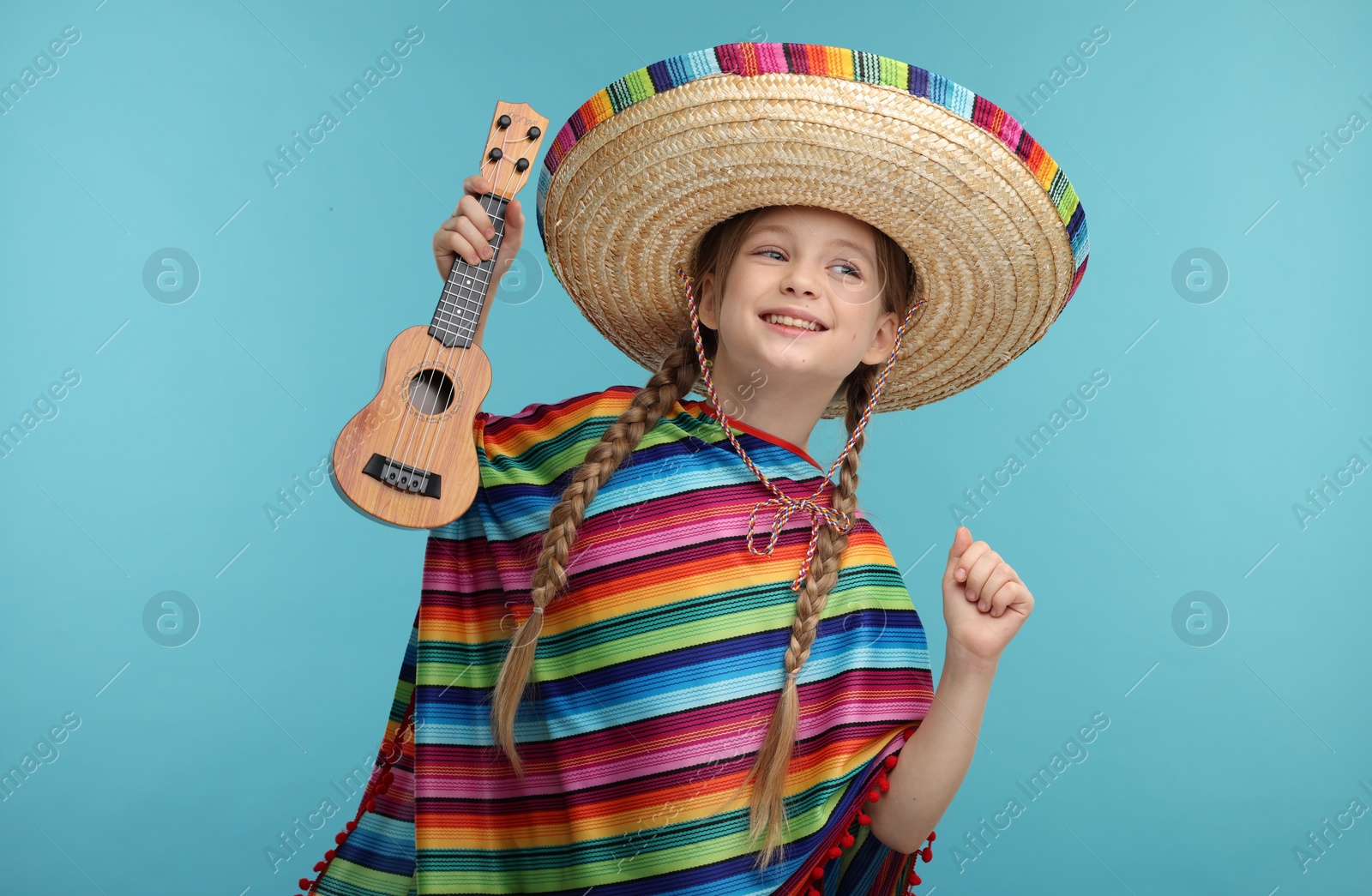 Photo of Cute girl in Mexican sombrero hat and poncho with ukulele on light blue background